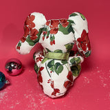White stuffed elephant toy with red and green floral pattern and green bow back in a red background.