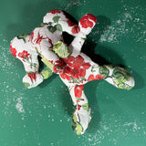 White stuffed elephant toy with red and green floral pattern and green bow in a green background.