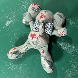 Floral patterned stuffed elephant toy with a blue and white bow with green  background.
