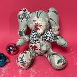 Floral patterned stuffed elephant toy with a blue and white bow in a red background.