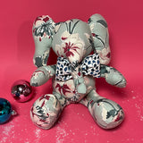 Floral patterned stuffed elephant toy with a blue and white bow in a red background.