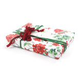 Side view of gift wrapped in red geranium wrapping paper with green ribbon and gift tag.