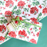 Styled display of red geranium wrapping paper with green ribbon and gift tag.