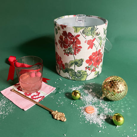 an acrylic ice bucket covered in geranium fabric and surrounded by a cocktail and festive decorations. 