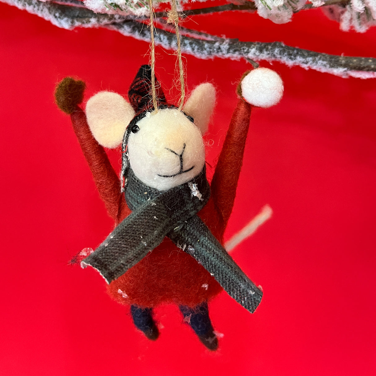 Cute felt mice ornament wearing a red sweater and grey scarf against a red background.