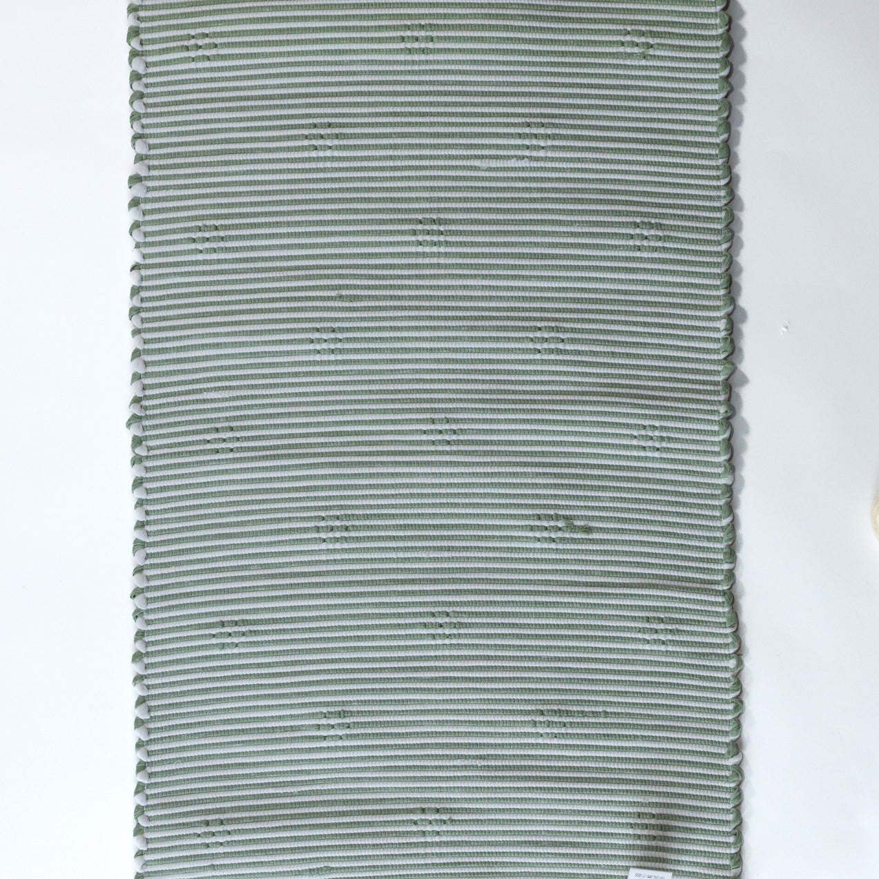 the reverse side of A rectangular green accent rug with small daisy shaped accents scattered across it. 