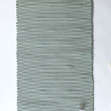 the reverse side of A rectangular green accent rug with small daisy shaped accents scattered across it. 