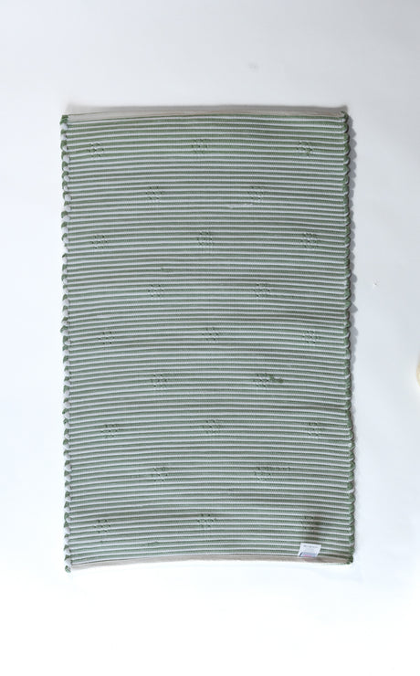 the reverse side of A rectangular green accent rug with small daisy shaped accents scattered across it. 