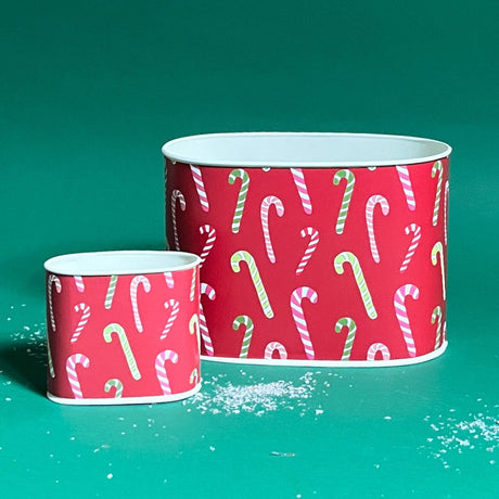 Two decoupage Dancing Candy Canes Christmas caddies with a candy cane pattern, one large and one small, placed on a green background with some decorative snow on the floor.