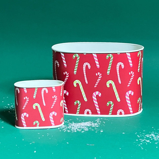 Two decoupage Dancing Candy Canes Christmas caddies with a candy cane pattern, one large and one small, placed on a green background with some decorative snow on the floor.