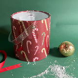 Dancing Candy Canes is a red acrylic Christmas ice bucket covered in a candy can motif fabric with faux snow and Christmas decorations in the image foreground.