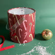 Dancing Candy Canes is a red acrylic Christmas ice bucket covered in a candy can motif fabric with faux snow and Christmas decorations in the image foreground.