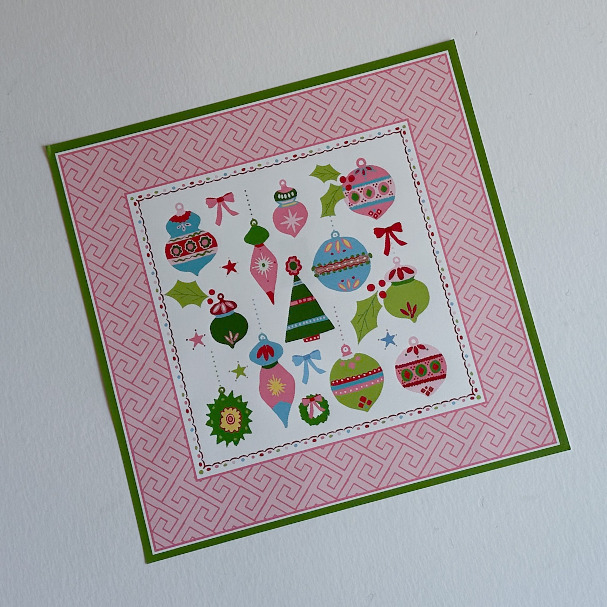 square pink paper placemats with colourful ornaments motifs in the center surrounded by a pink and green border. 