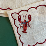 Detail of embroidered blue blow lobster on a linen cocktail napkin
