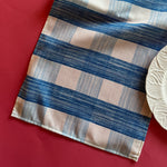 The Gin Lane cloth table runner is a gingham print in Swedish Blue shown on a red background with a white dinner plate