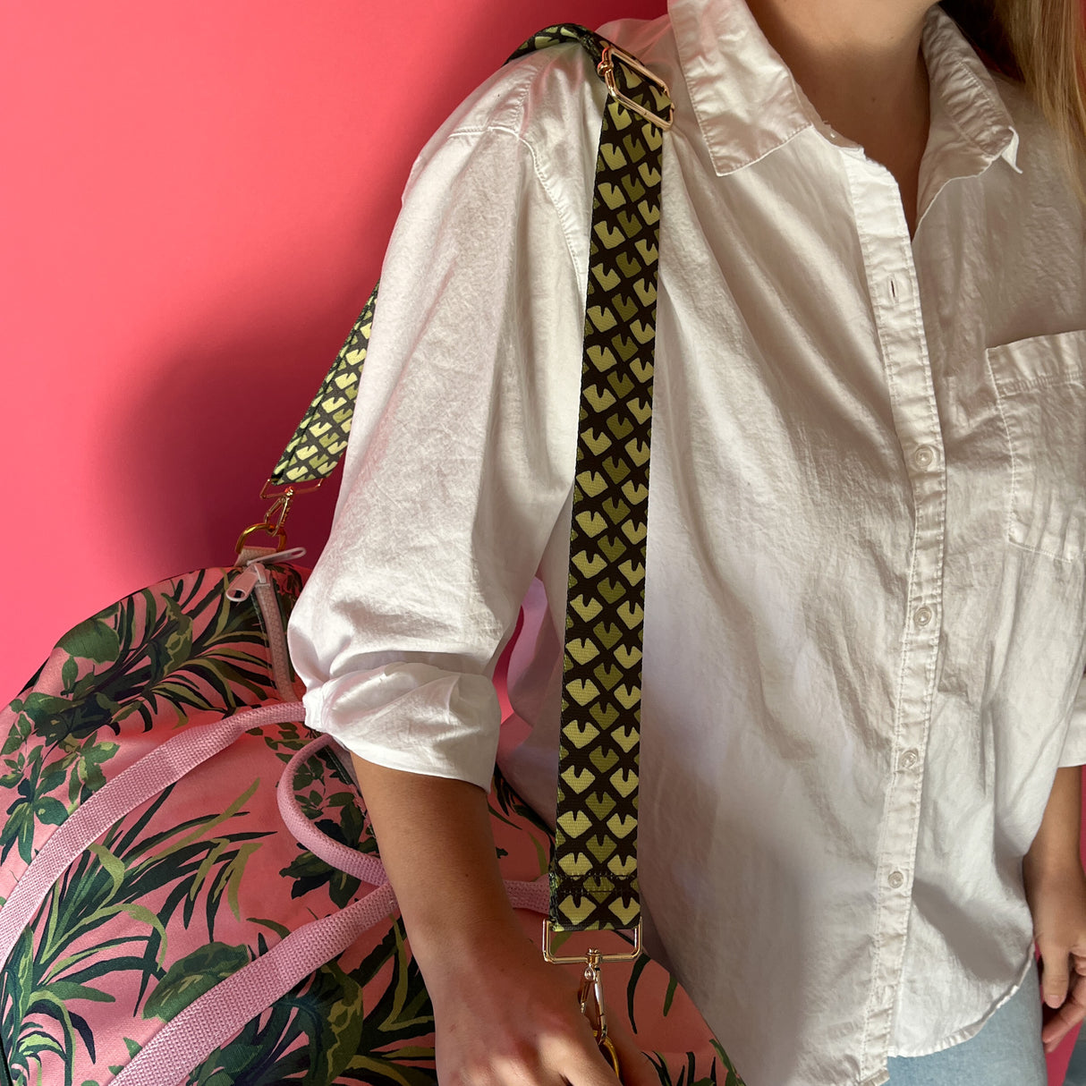Detail shot of the Jungle Road pink and green canvas duffle bag being used with a detachable shoulder strap