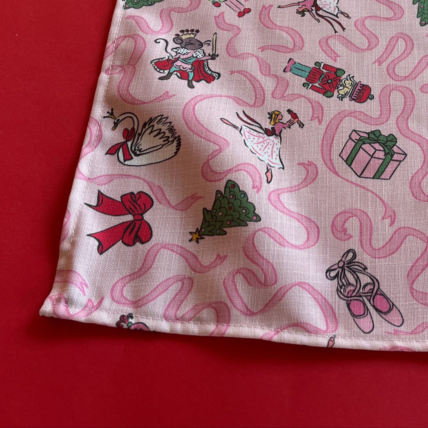 Detailed view of a pink Christmas cloth table runner with ribbons and scenes from The Nutcracker