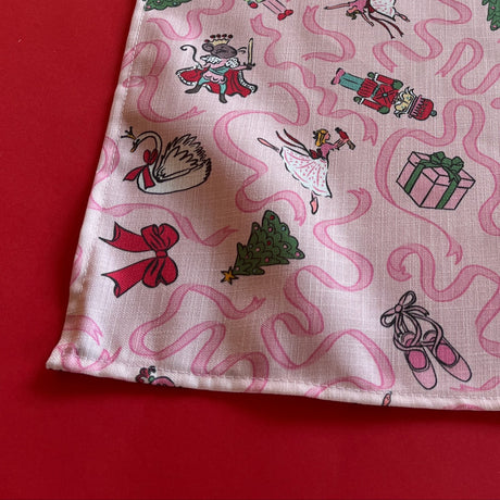 Detailed view of a pink Christmas cloth table runner with ribbons and scenes from The Nutcracker