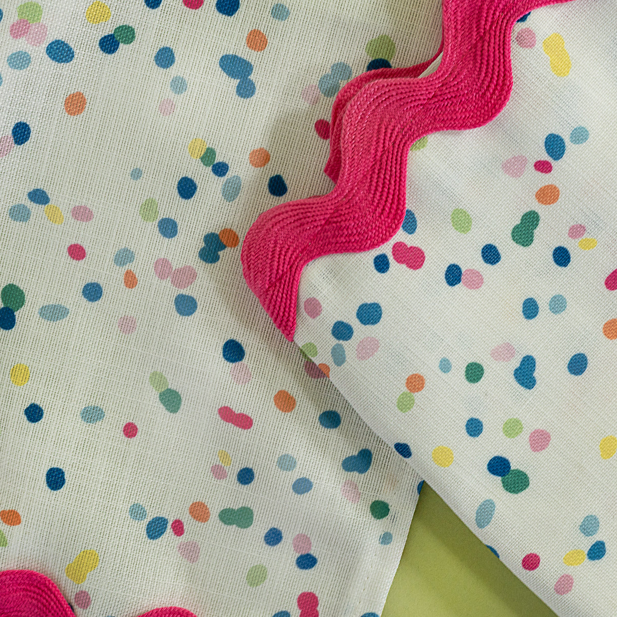 close up of a confetti multicolor fabric napkin with ric rac trim from Madcap Cottage on a light green background.
