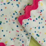 close up of a confetti multicolor fabric napkin with ric rac trim from Madcap Cottage on a light green background.