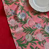 Detailed view of Shell Seekers cloth Table Runner features colorful shells, pink ribbons and green foliage on a pink background
