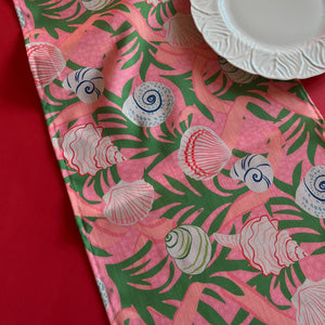 Detailed view of Shell Seekers cloth Table Runner features colorful shells, pink ribbons and green foliage on a pink background