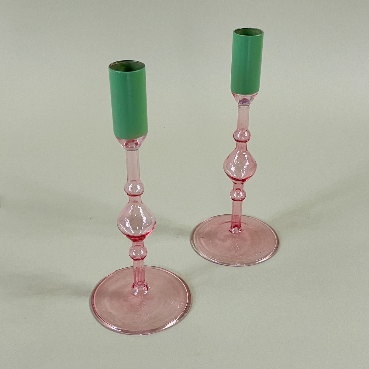 Pair pink glass candleolders with green tops on a light green background