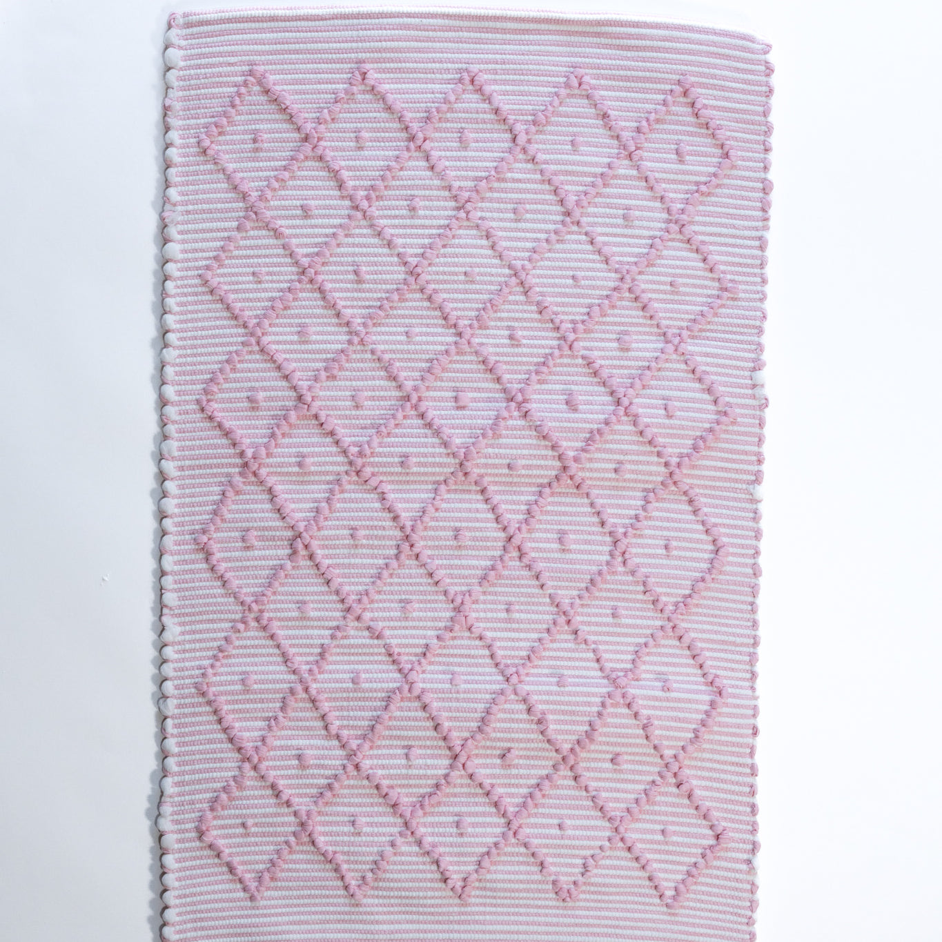 A madcap cottage cotton pink accent rug with a diamond pattern on the front 