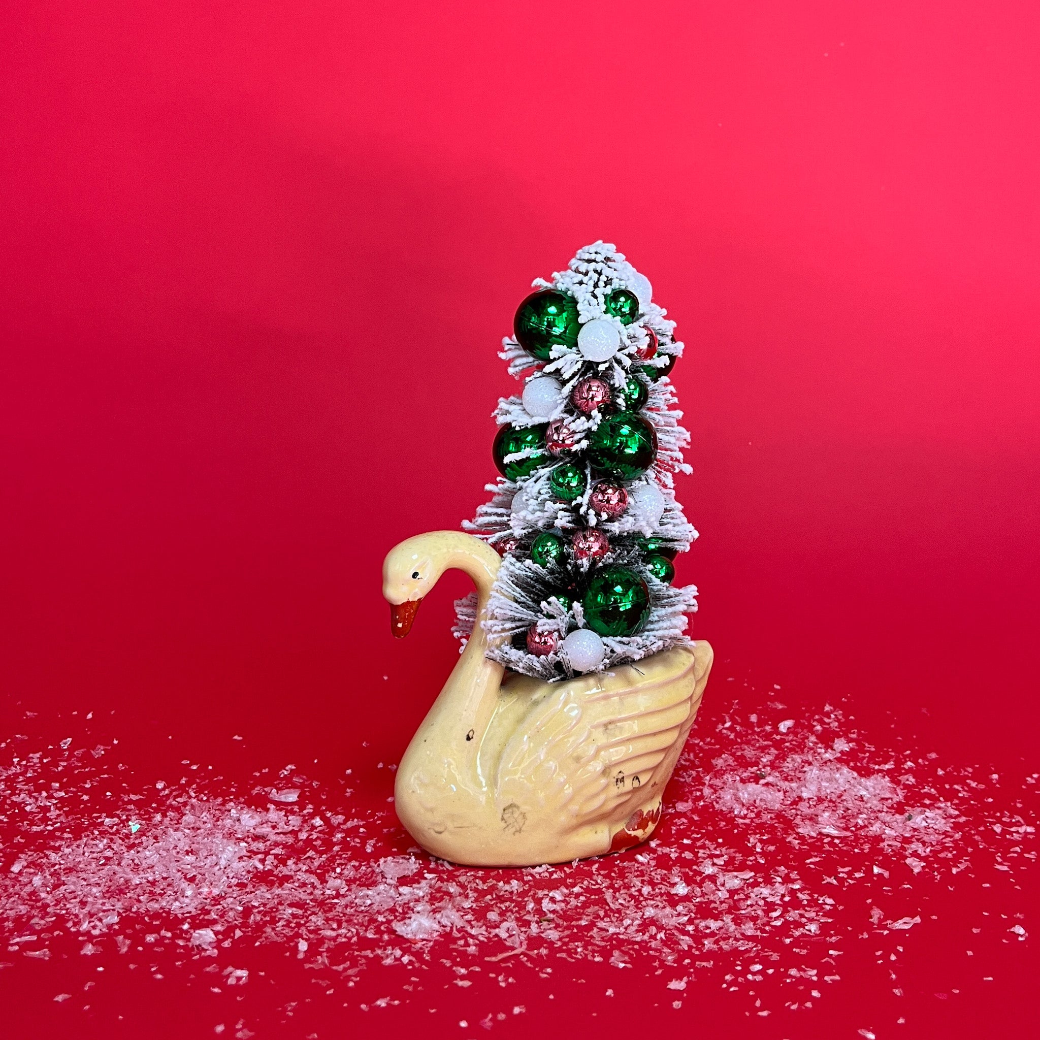A yellow coloured Vintage Distressed White Ceramic Swan centerpiece with a Flocked Christmas Tree inside it against a red background. 