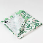 Close-up of a folded cloth napkin with a green and pink chinoiserie floral pattern and light green scalloped trim.