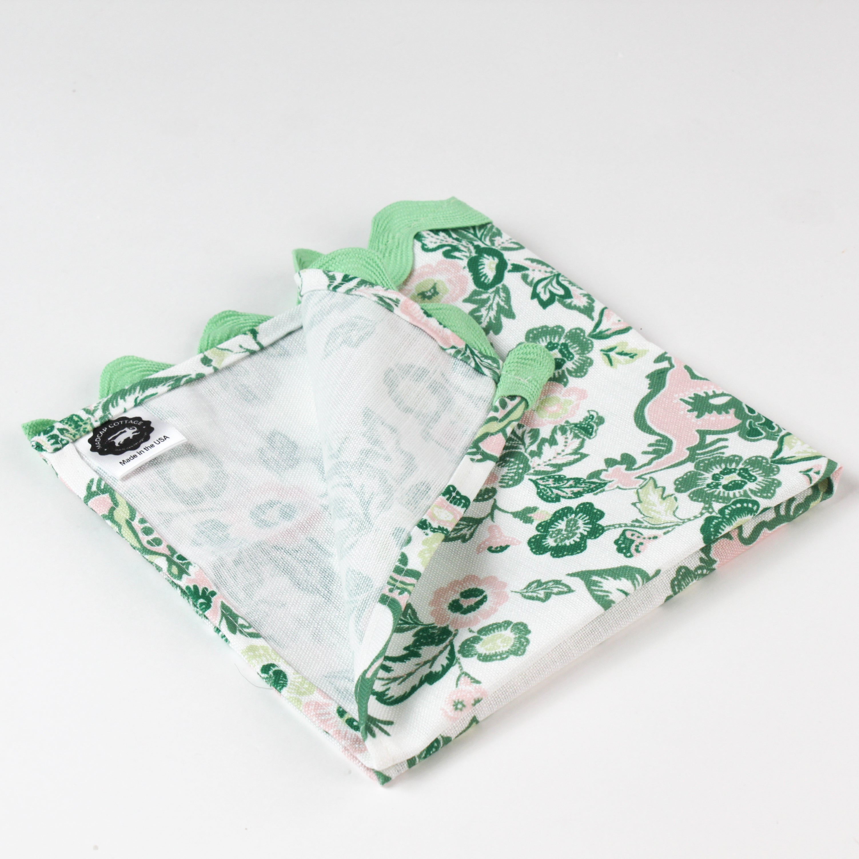 Close-up of a folded cloth napkin with a green and pink chinoiserie floral pattern and light green scalloped trim.