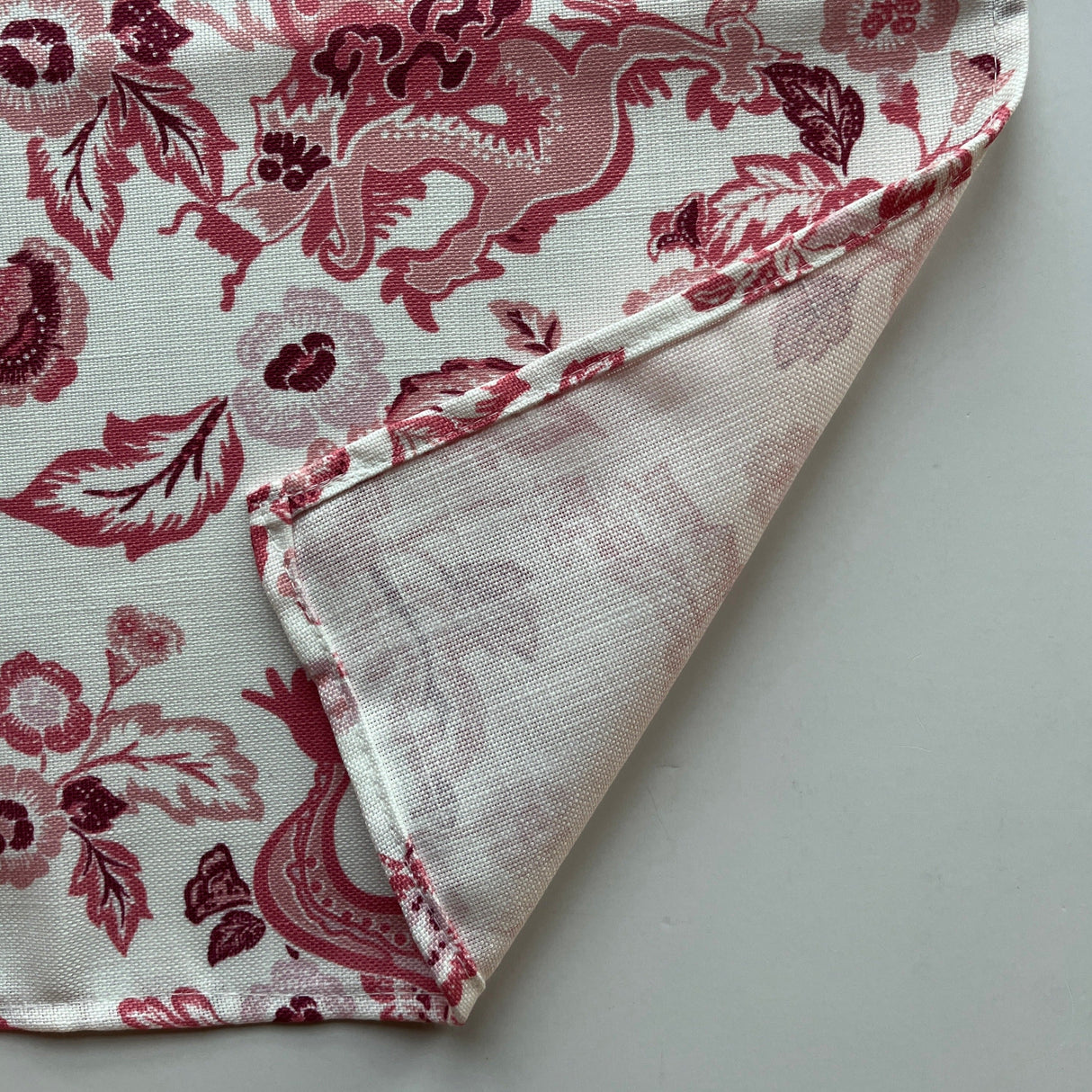 Close up of the hem of the East of the Sun chinoiserie cloth dinner napkin shown in red