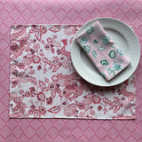 East of the Sun red chinoiserie placemats with a floral pattern, displayed on a table with a plate and a napkin.