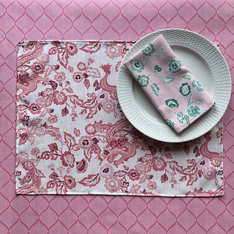 East of the Sun red chinoiserie placemats with a floral pattern, displayed on a table with a plate and a napkin.