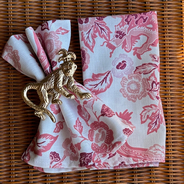 East of the Sun pattern in red dinner napkin in a gold monkey napkin ring n a rattan surface.