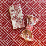 Paper napkin ring around a gathered fabric napkin in the East of the Sun pattern, shown in red.