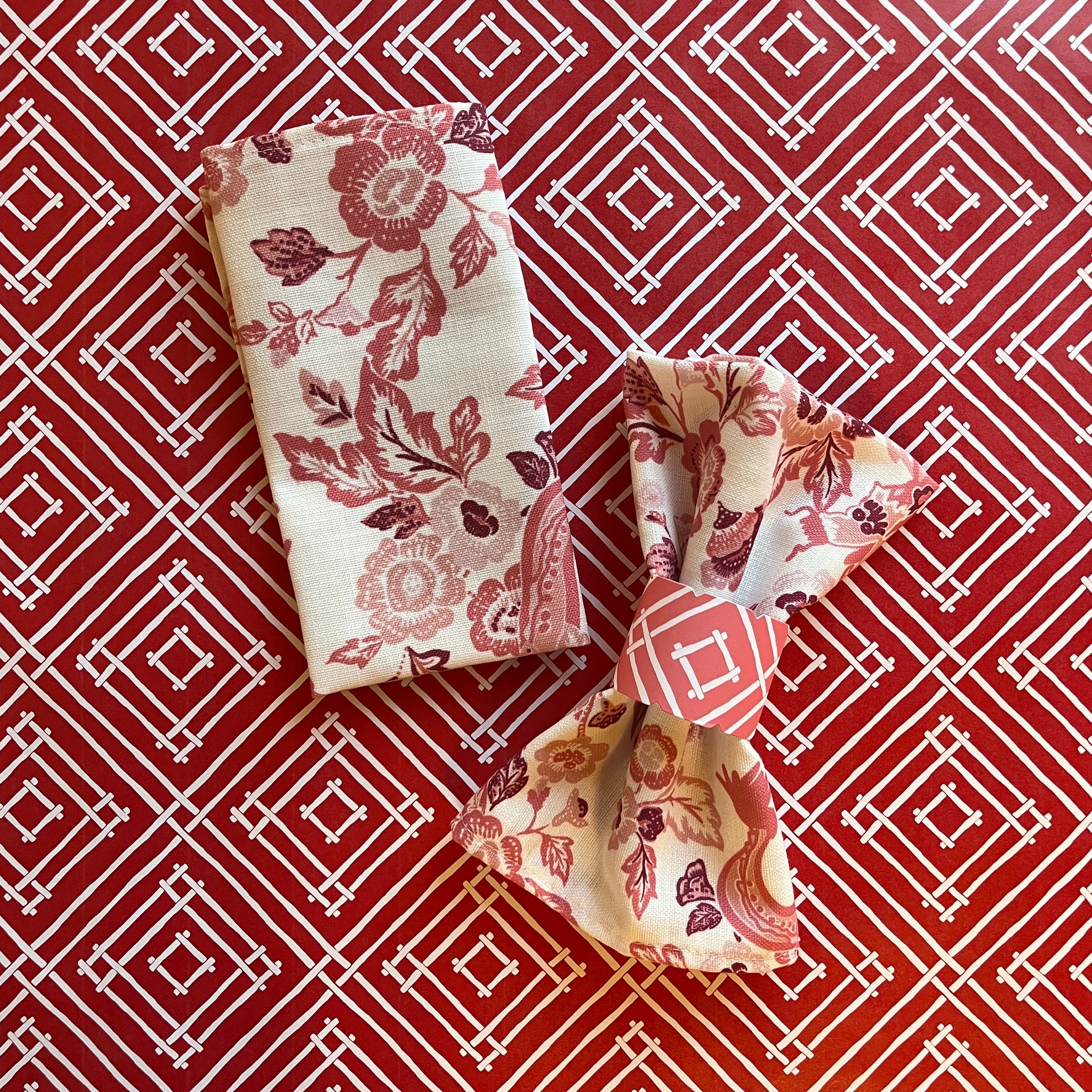 Paper napkin ring around a gathered fabric napkin in the East of the Sun pattern, shown in red.