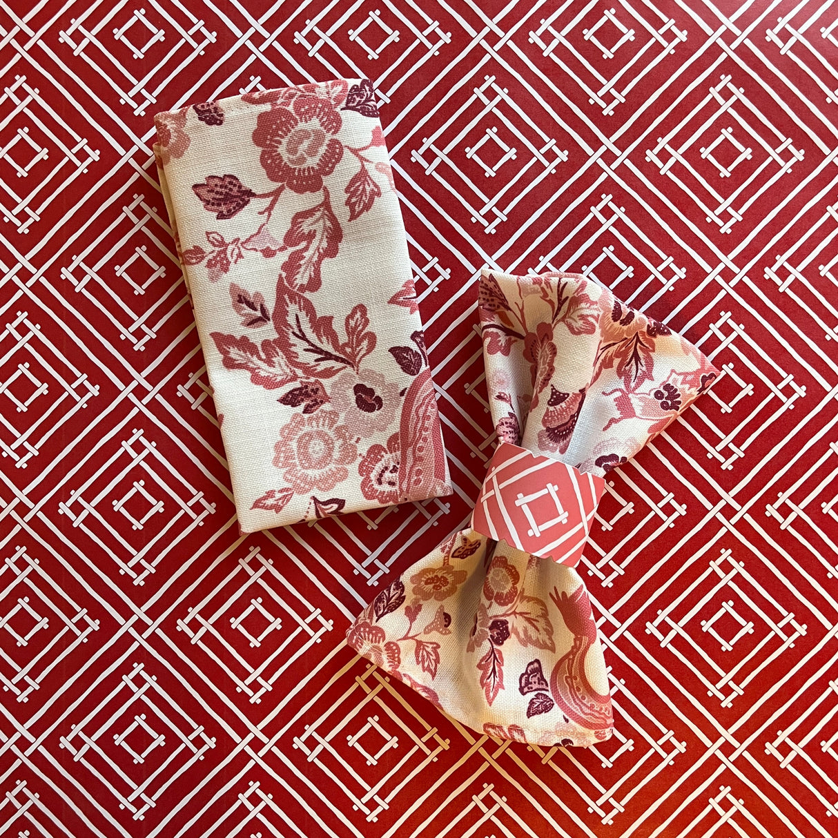 Paper napkin ring around a gathered fabric napkin in the East of the Sun pattern, shown in red.