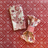 Paper napkin ring around a gathered fabric napkin in the East of the Sun pattern, shown in red.