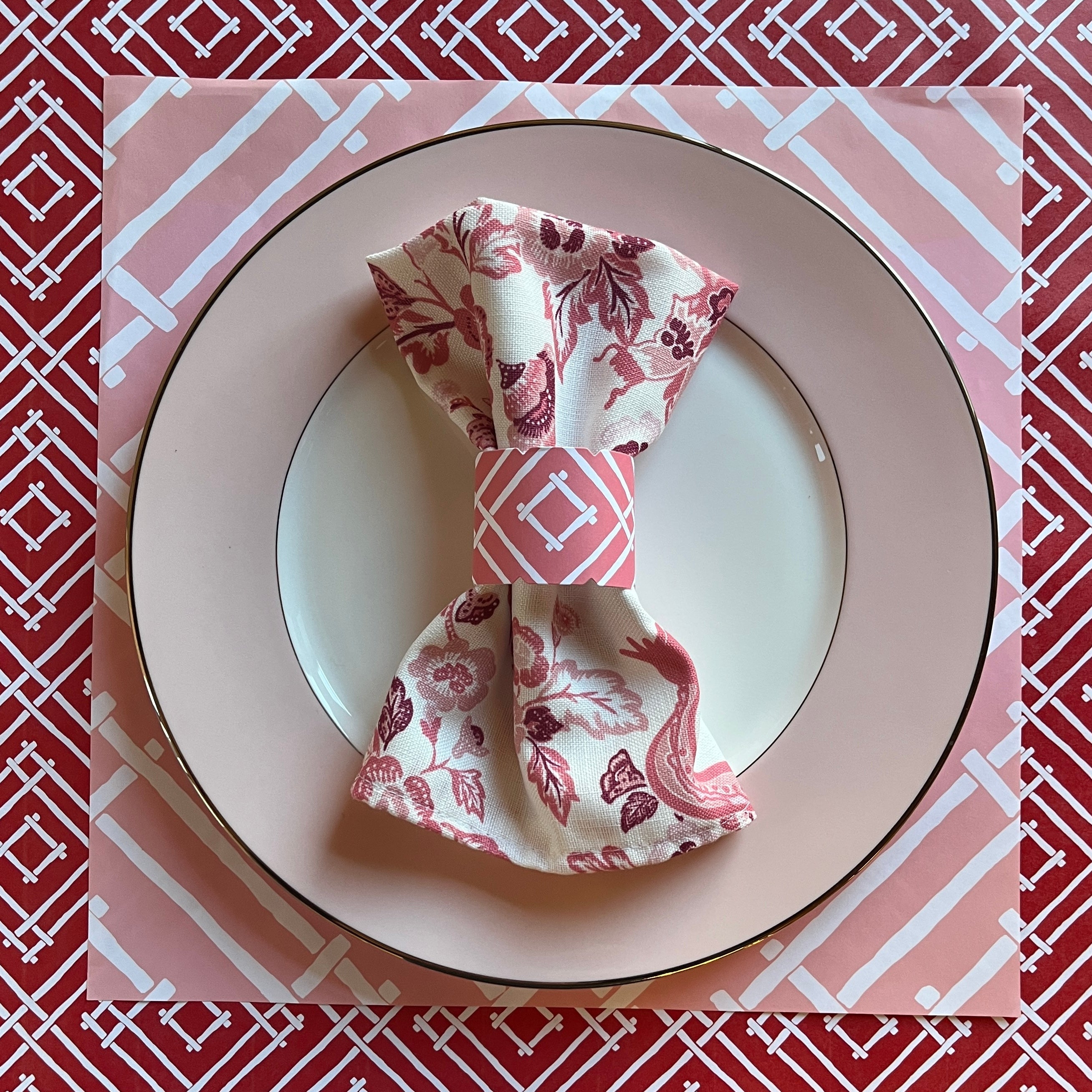 Layered placemats in reds and pinks with a light pink china plate on top, holding our East of the Sun chinoiserie cloth dinner napkin