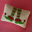 A white and green christmas throw pillow featuring a large motif of elves feet wearing stripey socks and green shoes