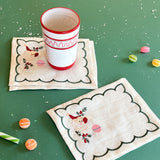 Embroidered Jolly Santa linen cocktail napkins with a cup and candies on a green background