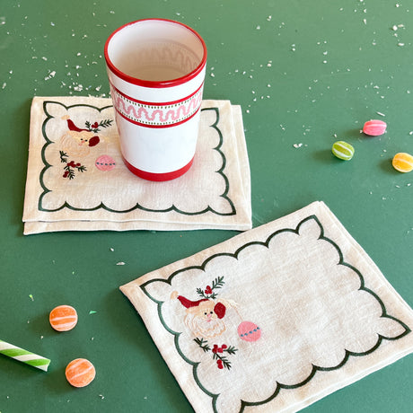 Embroidered Jolly Santa linen cocktail napkins with a cup and candies on a green background