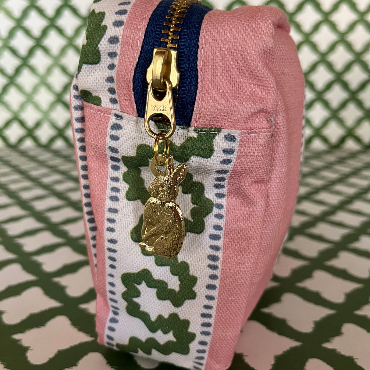 Pull detail of Harbor Trail toiletry bag in Bahama pink with a green ribbon and blue dash motif.