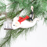 A felt mouse ornament hangs from a pine branch, posed as if flying with a red scarf, holding a feather pen and sheet music, and carrying a tiny black lantern on its back.