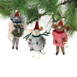 Three festive felt mouse ornaments dressed in fuzzy holiday outfits and Santa hats, holding Christmas decorations like string lights, a wreath, and a gold bell.