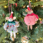 two festive felt mouse ornaments dressed in fuzzy holiday outfits and Santa hats, holding Christmas decorations like string lights, and a gold bell.