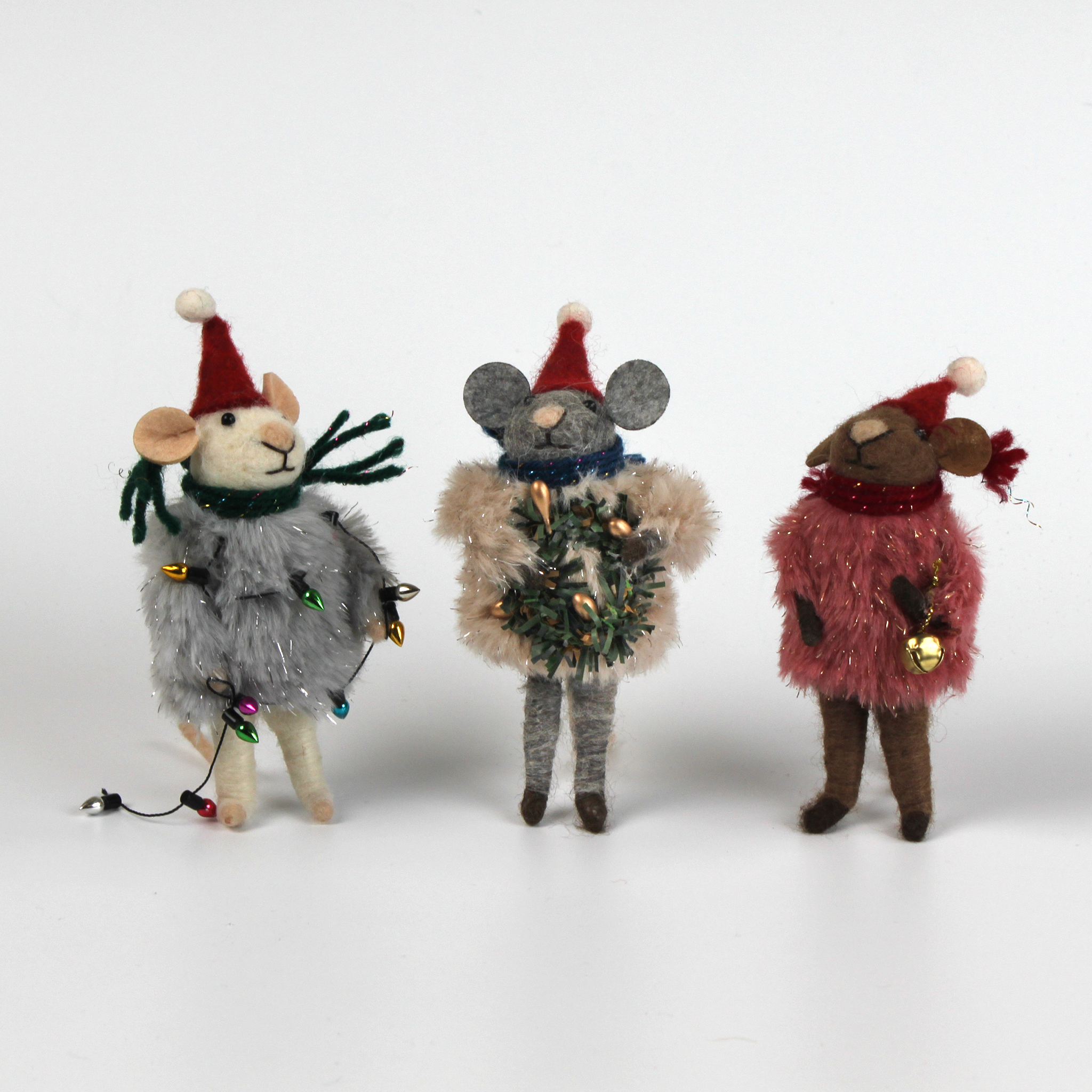 Three festive felt mouse ornaments dressed in fuzzy holiday outfits and Santa hats, holding Christmas decorations like string lights, a wreath, and a gold bell.