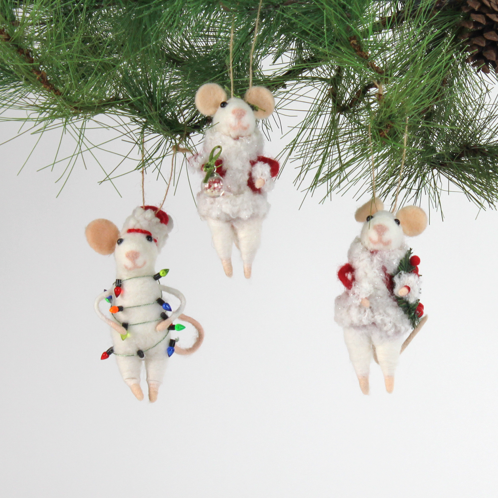 Three white felt mouse ornaments dressed in cozy winter outfits, one wrapped in colorful holiday lights, one holding a Christmas wreath, and one holding a festive ornament