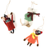 back of Three felt mouse ornaments dressed for winter—one in a red coat and plaid hat tossing a snowball, one in an orange coat with a yellow scarf holding a snowball, and one in a green sweater holding red berries—lying in white surface.
